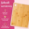 A close-up of a bamboo cutting board with a heart-shaped cutout, set against a pink and white background with text describing its features. Produktbild-Vorschau