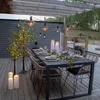 An outdoor dining area set up for an evening meal, with string lights and decorative trees. Produktbild-Vorschau