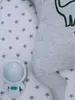 A baby's sleepsuit with a dinosaur print and an astronaut-shaped night light on a star-patterned sheet. Produktbild-Vorschau