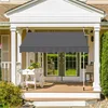 A dark gray awning is installed over a porch in front of a house. There is a white planter with flowers on the porch. Produktbild-Vorschau