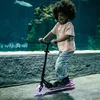 A young child rides a scooter with LED wheels in front of a large aquarium. Voir les images du produit