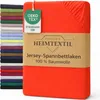 A folded red jersey fitted sheet is displayed prominently, with a stack of other folded sheets in various colors visible on the left. A product tag and a cardboard band with branding and product information are attached to the sheet. Produktbild-Vorschau