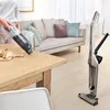 A person is using a handheld vacuum cleaner to clean crumbs from a wooden table, with a larger vacuum cleaner standing in the background. Produktbild-Vorschau