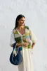 A woman wearing a crochet vest and dress, holding a bag. Produktbild-Vorschau