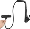 A hand holding a black pull-down kitchen faucet spray head, connected to the faucet body by a black hose. Náhled obrázku produktu