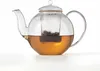 A glass teapot filled with amber-colored tea, with a tea infuser containing tea leaves inside. Produktbild-Vorschau
