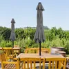 An outdoor patio setting with wooden tables and chairs, and two closed umbrellas. Produktbild-Vorschau