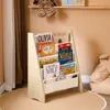 A children's bookshelf filled with books in a room with a rug and curtains. Produktbild-Vorschau