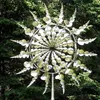 A kinetic wind spinner is displayed outdoors in a garden setting, with trees in the background. Anteprima dell’immagine prodotto
