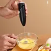 A person is using a black handheld electric frother to whisk eggs in a glass bowl. Produktbild-Vorschau