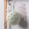 A crocheted ball ornament with small colorful pom-poms attached, hanging against a wall. Produktbild-Vorschau