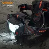 A black headlamp with the light on, sitting on a wet surface with water droplets. Podgląd zdjęcia produktu