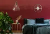 A bedroom with a red wall, a bed with blue and green bedding, a plant, and a gold side table. Náhled obrázku produktu