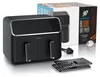 A black dual-chamber air fryer is displayed on a white background, with its packaging box visible behind it. A metal rack accessory is placed in front of the air fryer. Produktbild-Vorschau