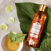 A bottle of shower oil is placed next to a bowl of oil and some leaves, with petals scattered around. Anteprima dell’immagine prodotto