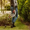 A person is holding an electric hedge trimmer in a garden, preparing to trim a bush. Voir les images du produit