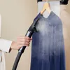 A person is using a garment steamer on a blue dress hanging on a hanger. Produktbild-Vorschau