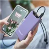 A person is holding a smartphone and a purple power bank that is charging the phone. Voir les images du produit