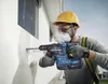 A construction worker is drilling a hole in a white wall with a Bosch rotary hammer drill. Voir les images du produit
