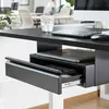 A close-up view of a black under-desk drawer with a laptop and remote control inside, set in a modern office environment. Voir les images du produit