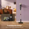 A cordless vacuum cleaner is shown standing upright against a purple wall, with a close-up inset of its cleaning head. The background includes a living room setting with a teddy bear on a chair and a cabinet. Produktbild-Vorschau