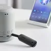 A Ugreen Bluetooth receiver is plugged into a white speaker, with a smartphone in the background displaying music controls. Anteprima dell’immagine prodotto