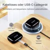 Two black wireless earbuds cases are shown on a wooden surface. One is connected to a USB-C cable, and the other is placed on a wireless charging pad. Produktbild-Vorschau