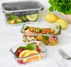 Three glass food storage containers filled with various foods, set on a light-colored surface with lemons and lettuce in the background. Produktbild-Vorschau