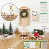 A collection of miniature Christmas decorations, including a wooden door, wreath, trees, signs, and other accessories, arranged on a wooden floor with scattered artificial snow. Produktbild-Vorschau