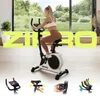 A woman is using a stationary bike in a bright, modern room with a large window overlooking a lush green landscape. Below the main image are four smaller inset images showcasing different features of the bike. Produktbild-Vorschau