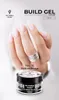 A hand with light pink gel nails is shown, with a jar of Victoria Vynn Build Gel in Delicate Rouge in the foreground. Náhled obrázku produktu