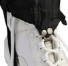 Close-up view of a black gaiter attached to a white sneaker with metal snaps. Náhľad obrázku produktu