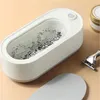 An ultrasonic cleaner is shown with water and some debris inside, next to a razor and a tin. A lid for the cleaner is also visible. Voir les images du produit
