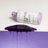 A bottle of Olaplex No.4P Blonde Enhancer Toning Shampoo is shown lying on its side, with purple shampoo dripping from its cap onto a purple surface below. Anteprima dell’immagine prodotto
