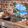A kitchen counter with a stovetop, cooking utensils, and vegetables, with a decorative glass panel featuring a landscape scene behind it. Produktbild-Vorschau