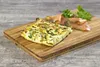 A slice of frittata with smoked salmon and parsley on a wooden cutting board. Produktbild-Vorschau