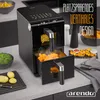 A black air fryer is shown on a kitchen counter, with food being cooked inside and displayed around it. Produktbild-Vorschau