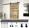 A sliding barn door with a black metal track and hardware, displayed against a white wall with a framed picture of a tree and a plant in a pot. Produktbild-Vorschau
