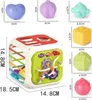 A multi-colored activity cube toy with various shapes and interactive elements, surrounded by smaller individual toy pieces with size dimensions indicated. Produktbild-Vorschau