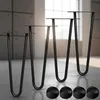 Four black hairpin legs are displayed on a concrete floor in front of a window with natural light. Four black circular caps are also visible in the foreground. Produktbild-Vorschau