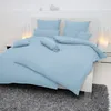 A neatly made bed with light blue bedding, including a duvet and pillows, set against a white headboard and wall. Produktbild-Vorschau