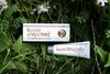A box and tube of White Mumio cosmetic product are placed on a background of green grass and small purple flowers. Produktbild-Vorschau