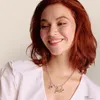 A woman wearing a white shirt and a necklace with charms. Anteprima dell’immagine prodotto