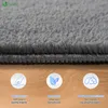 Close-up of a gray carpet with three circular icons and text below, set against a wooden background. Produktbild-Vorschau