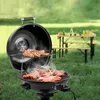 A barbecue grill with meat cooking on it, set up outdoors in a grassy area with a picnic table in the background. Produktbild-Vorschau