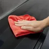 A hand is wiping a dark, glossy surface with a red microfiber cloth. Produktbild-Vorschau