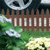 A brown garden fence is shown in a garden setting with flowers and a car tire in the background. Náhľad obrázku produktu