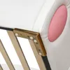 A close-up view of the corner of a white upholstered bed frame with gold metal accents and white plastic protective caps. A pink oval shape is visible on the right side of the frame. Produktbild-Vorschau