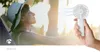 A person wearing a hat enjoys a sunny day while a white hand-held fan is used to cool them. Produktbild-Vorschau