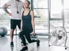A woman is performing a lunge exercise with dumbbells in a gym, with a fan in the foreground. Voir les images du produit